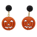 A pair of Halloween dangle earrings featuring round orange jack-o'-lantern cutouts with carved facial features, suspended from gold-tone chains with black round studs, shown against a plain white background. - Lilylin Designs