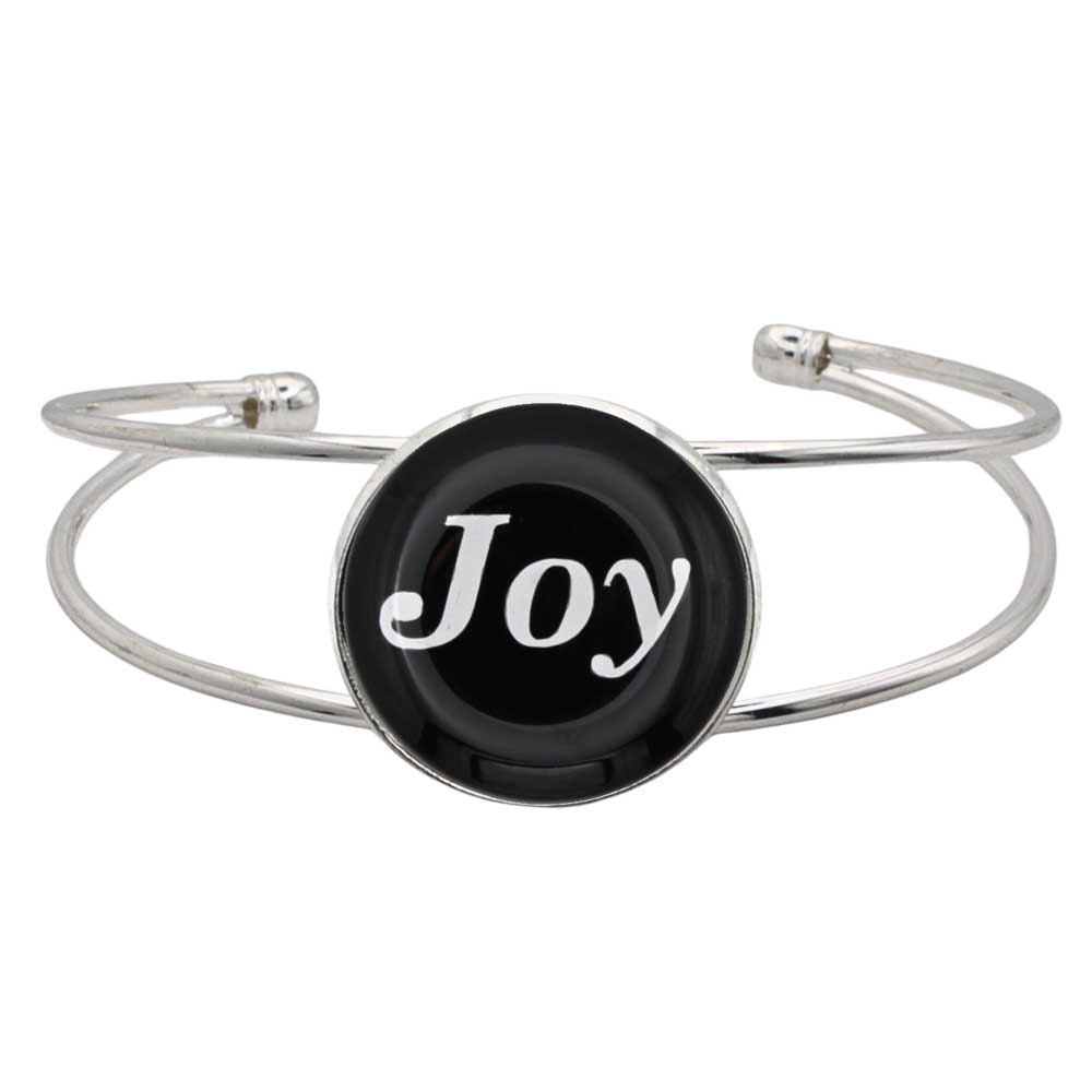 A silver-toned metal cuff bracelet featuring a round black disc with the word 'Joy' in white script, shown on a plain white background.