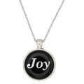 A silver chain necklace with a round pendant featuring a black background and the word 'Joy' in white script, shown on a plain white background - Lilylin Designs