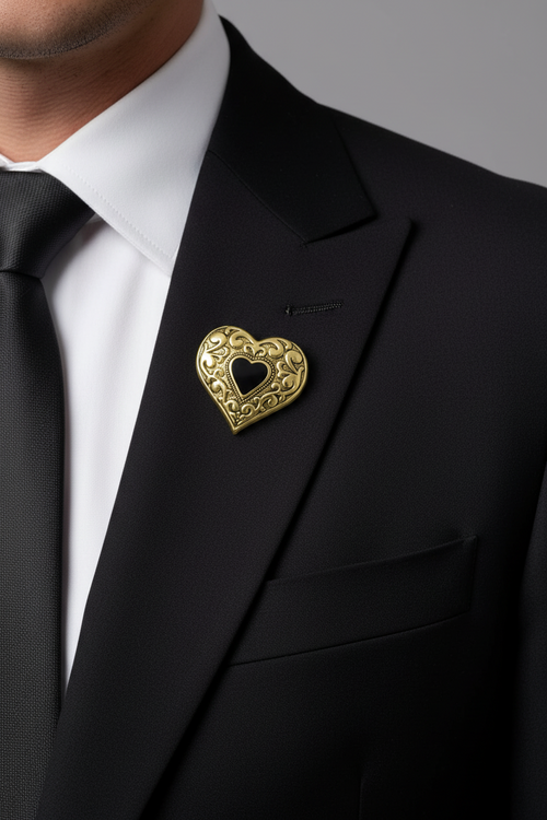 A close-up of a man wearing a black suit jacket, white dress shirt, black tie, and a gold heart-shaped brooch with an ornate filigree pattern and a smaller heart in the center. - Lilylin Designs
