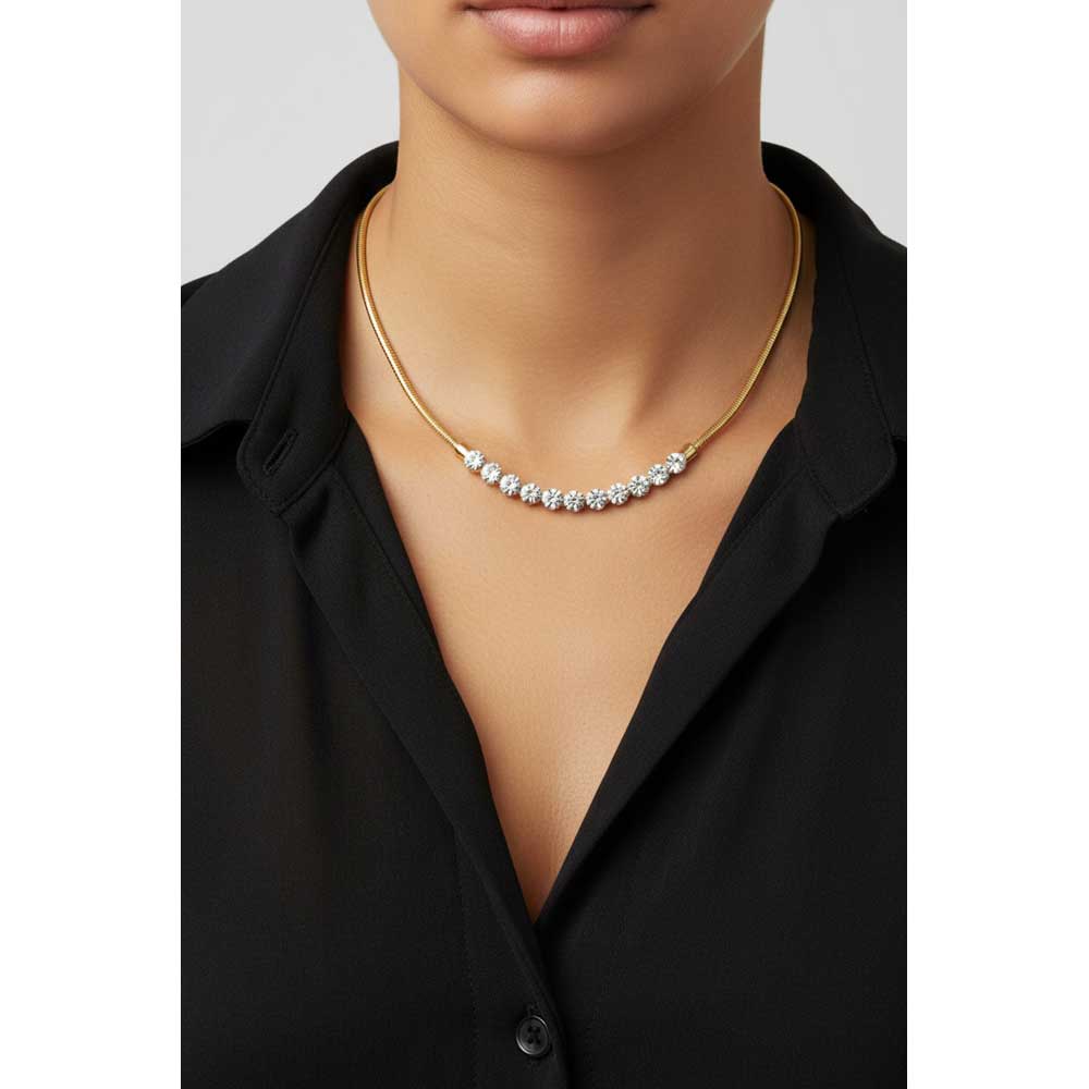 A close-up of a model wearing a delicate gold chain necklace with a curved row of clear gemstones across the chest, styled with a black collared shirt. Lilylin Designs