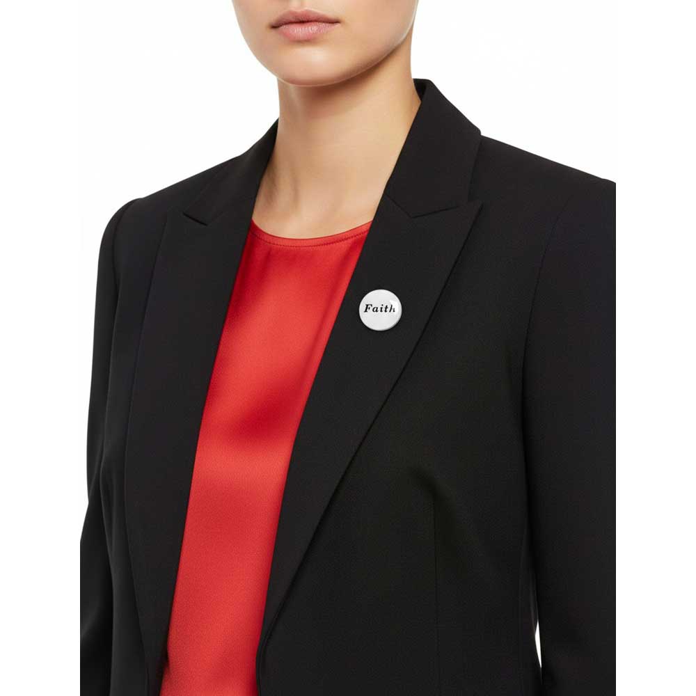 A close-up of a model wearing a black blazer over a bright red satin top, featuring a small round white button pin on the lapel with the word 'Faith' printed in black. Lilylin Designs