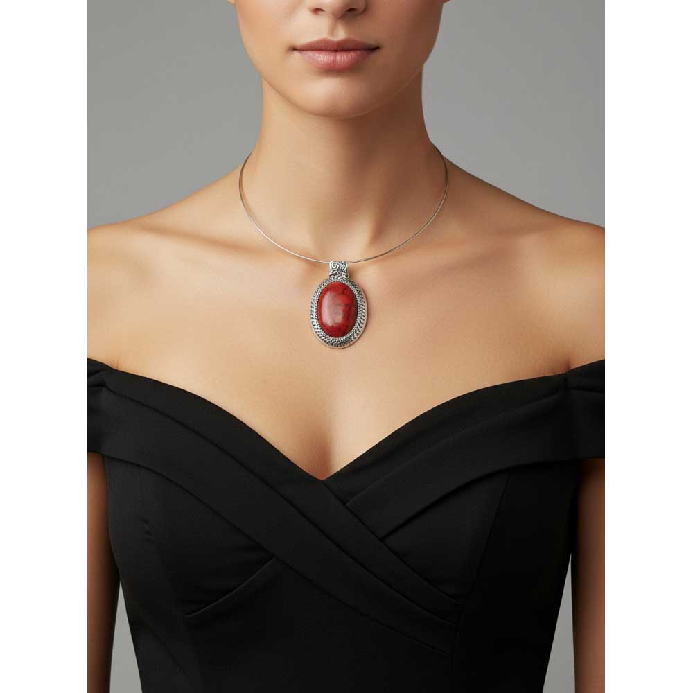 A close-up of a model wearing a silver-toned necklace with an oval red simulated turquoise pendant, paired with a black off-the-shoulder dress against a neutral gray background. Lilylin Designs
