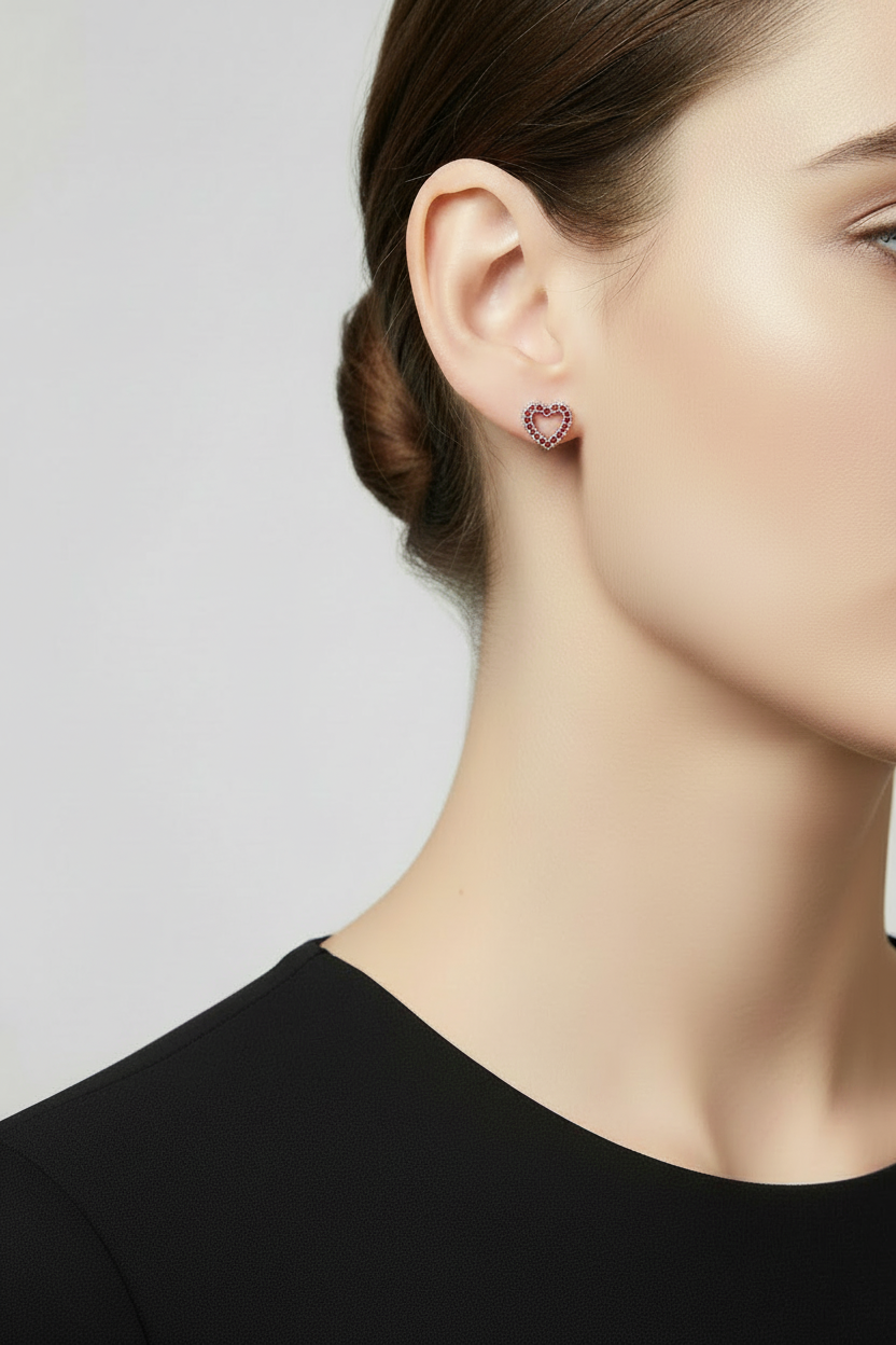 A close-up of a model's ear wearing a small heart-shaped stud earring with red crystals - Lilylin Designs