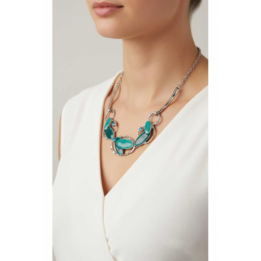 A close-up of a model wearing a silver statement necklace with turquoise and green stone accents, paired with a white V-neck top. Lilylin Designs