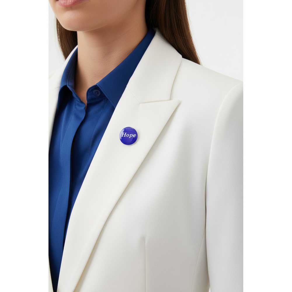 A close-up of a person wearing a white blazer over a blue collared shirt, with a small round blue pin reading 'Hope' on the lapel. Lilylin Designs