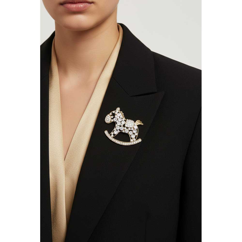 A close-up of a model wearing a black blazer over a beige satin V-neck top, featuring a gold and crystal-embellished rocking horse brooch on the lapel. Lilylin Designs