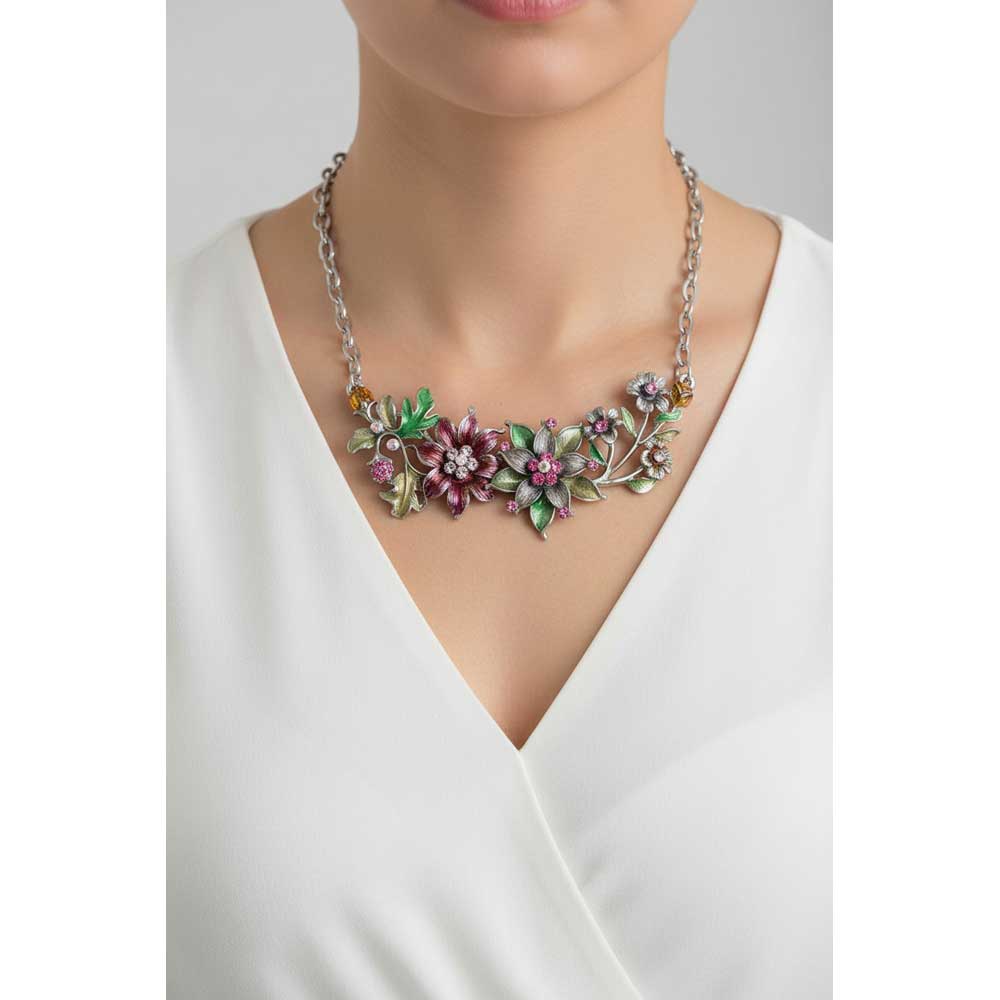A close-up of a model wearing a silver chain necklace with a detailed floral centerpiece in pink, purple, and green enamel - Lilylin Designs