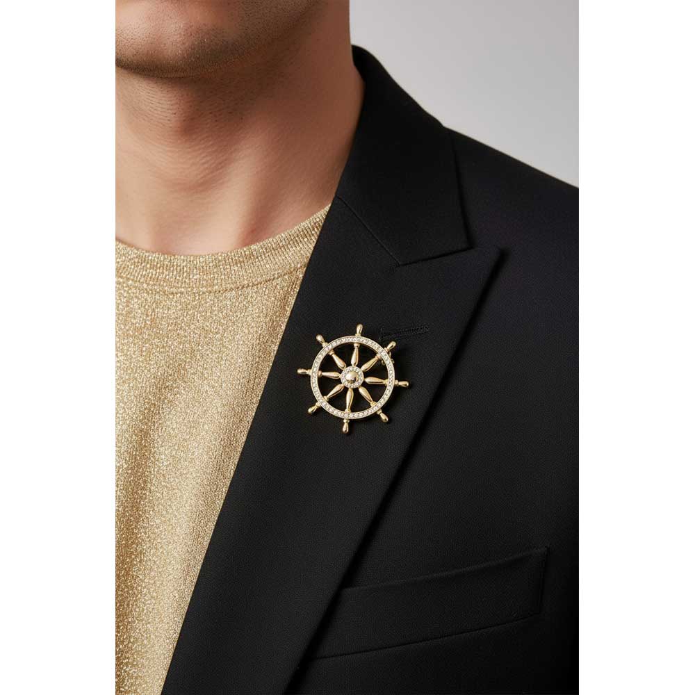 A gold ship's wheel brooch with small clear stones, pinned to the lapel of a black blazer worn over a textured gold shirt. Lilylin Designs