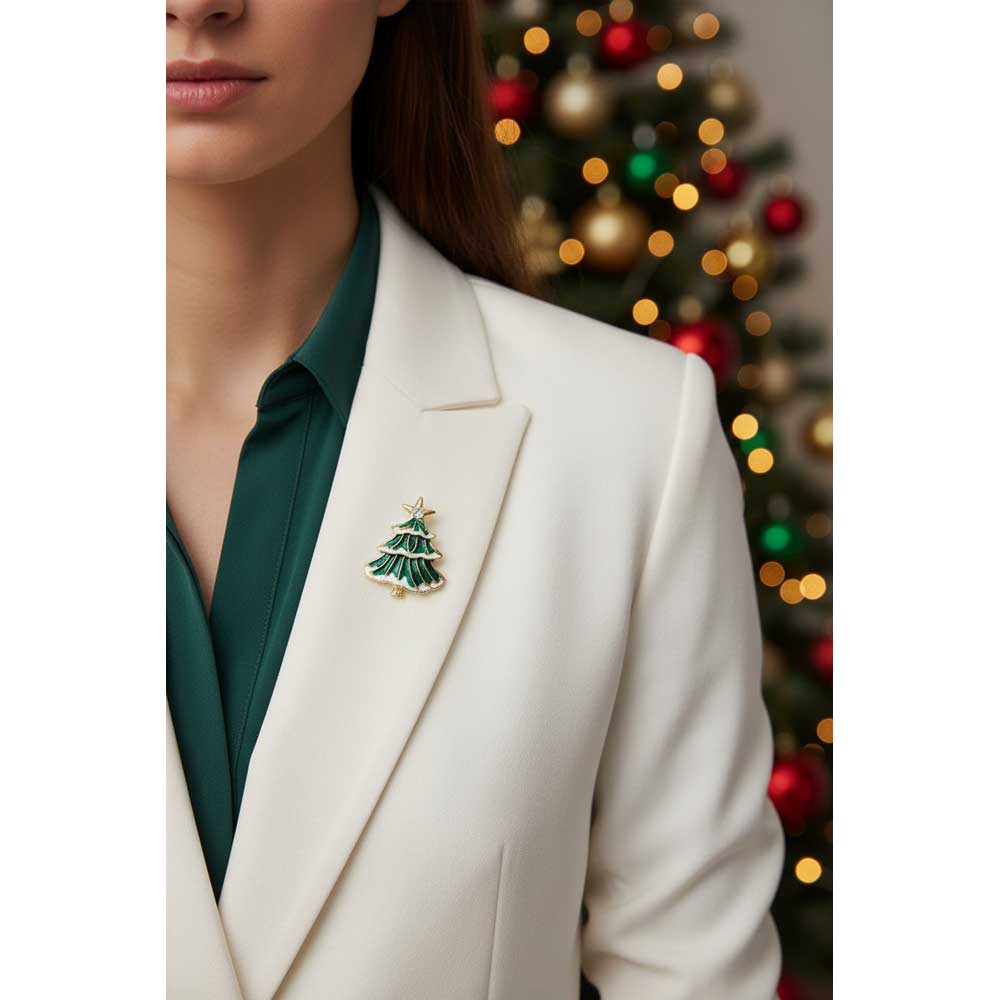 A woman wearing a white blazer and dark green shirt, featuring a small gold and green Christmas tree lapel pin on her left lapel, with a blurred Christmas tree in the background. Lilylin Designs
