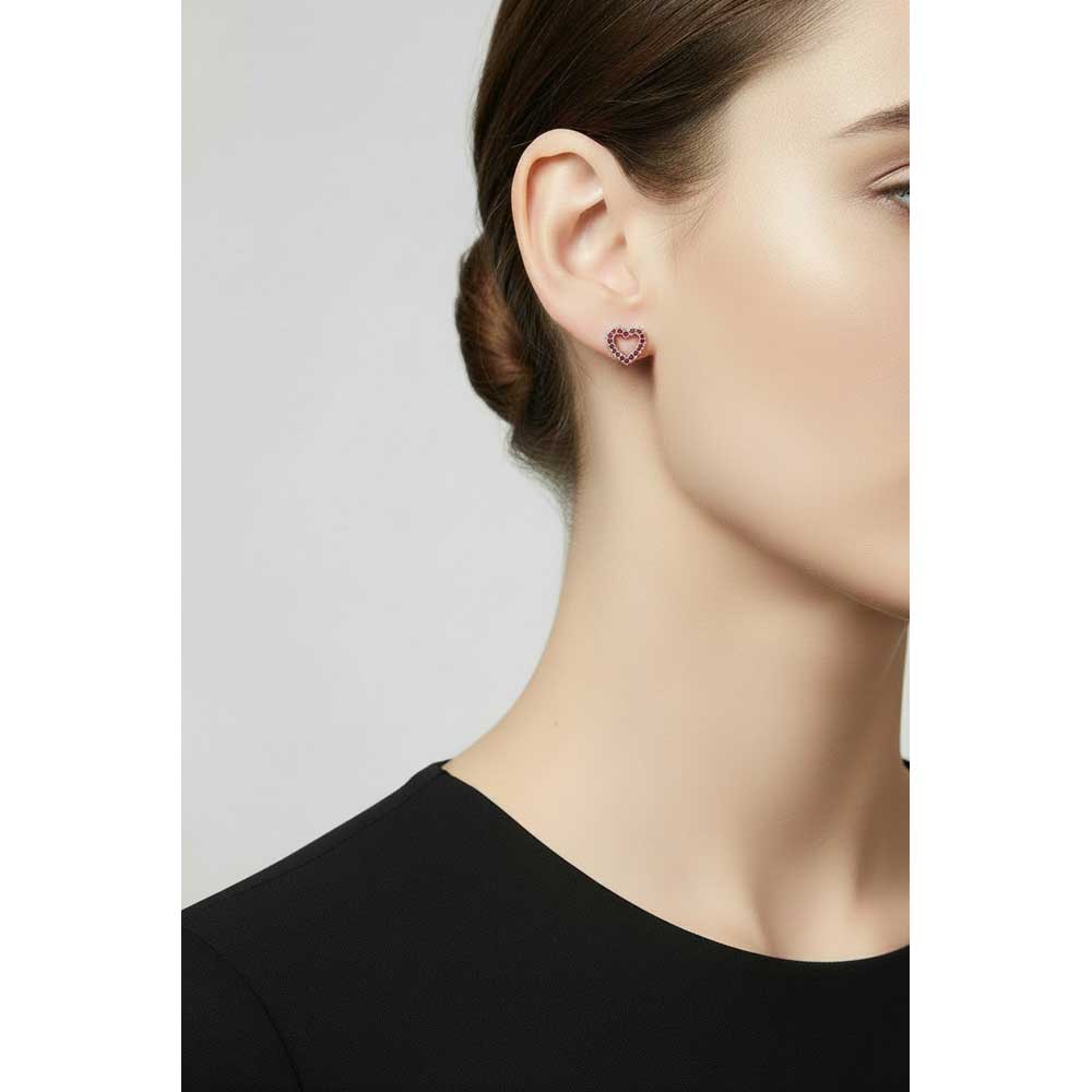 A close-up of a model's ear wearing a small heart-shaped stud earring with red crystals - Lilylin Designs