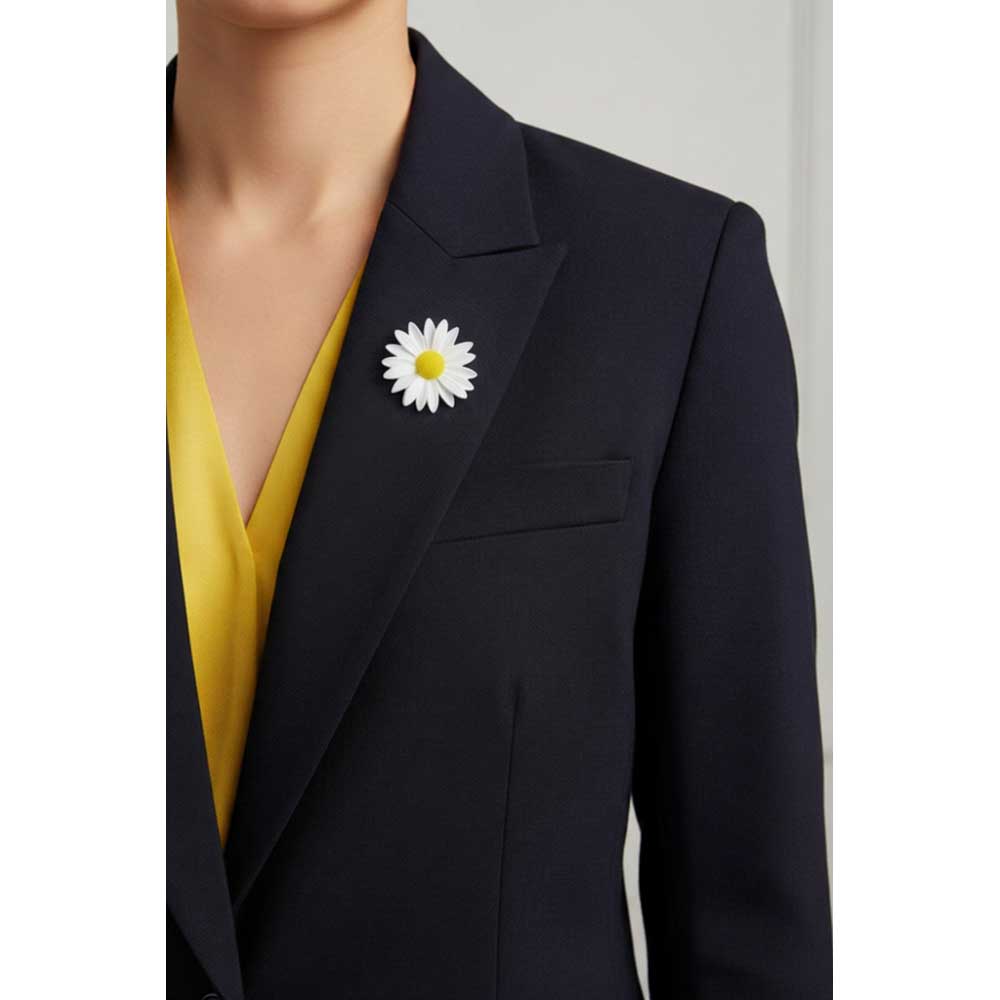 A close-up of a person wearing a dark navy blazer over a bright yellow V-neck top, featuring a white and yellow daisy brooch pinned to the left lapel. Lilylin Designs