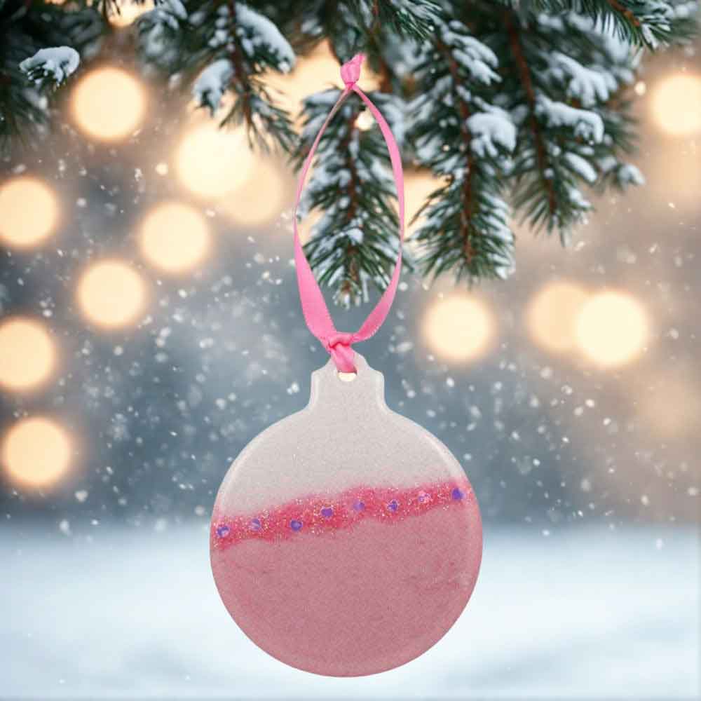 Pink Christmas ornament hanging on a tree branch with a blurred festive background | Lilylin Designs