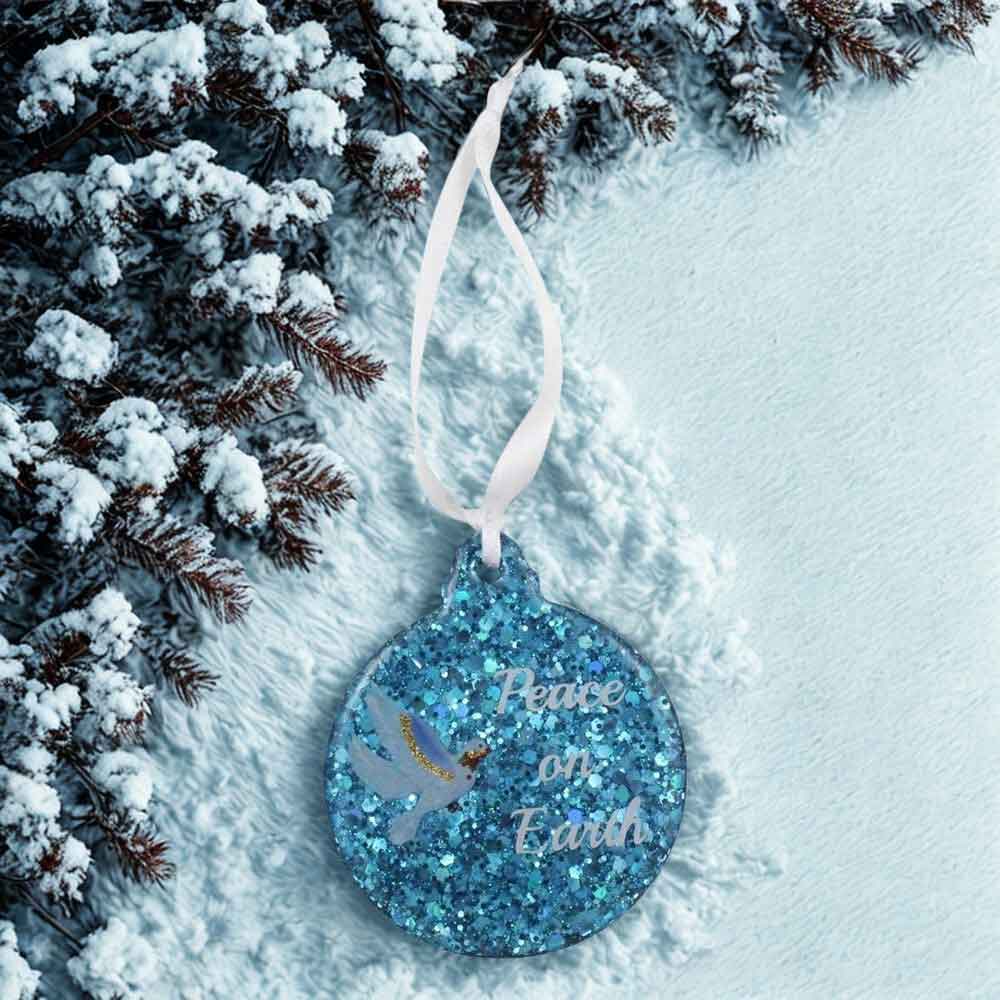 Blue glittery ornament with 'Peace on Earth' text hanging from a snowy branch. | Lilylin Designs