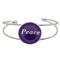 A silver-toned metal cuff bracelet featuring a round purple disc with the word 'Peace' printed in white script, shown on a plain white background – Lilylin Designs