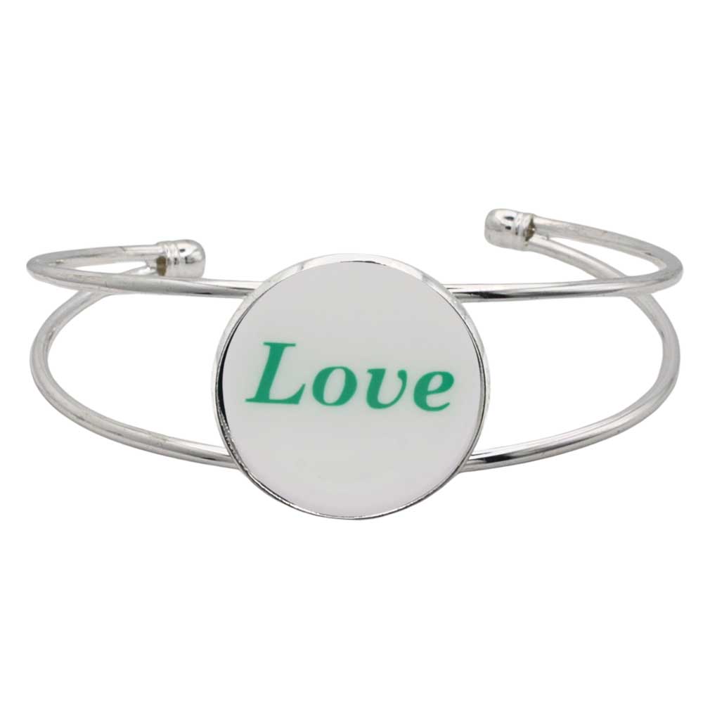 A silver-toned metal cuff bracelet featuring a round white disc with the word “Love” printed in green script, shown on a plain white background – Lilylin Designs