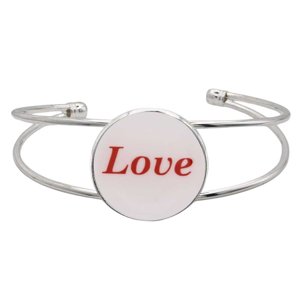 A silver-toned metal cuff bracelet featuring a round white disc with the word “Love” printed in red script, shown on a plain white background – Lilylin Designs