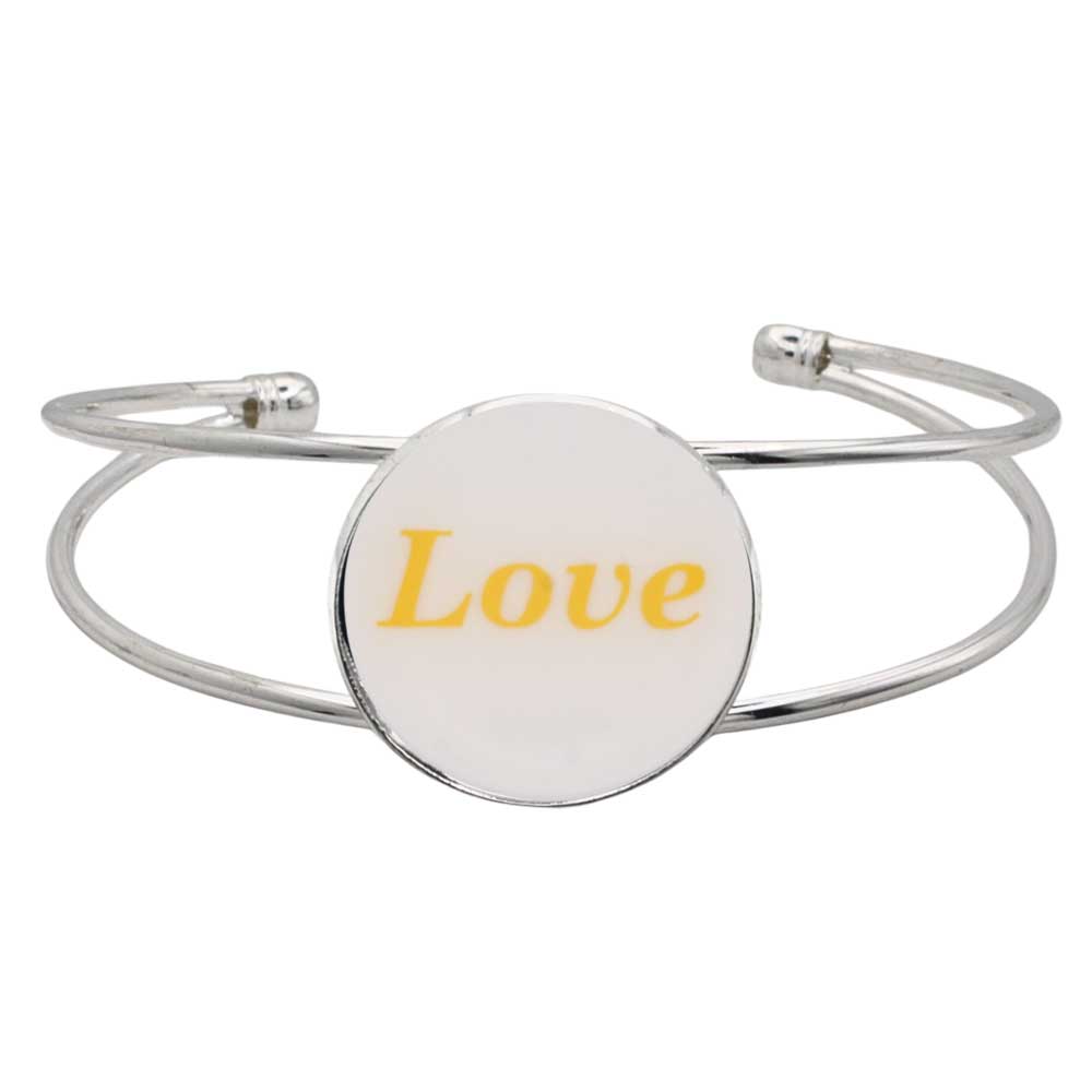A silver-toned metal cuff bracelet featuring a round white disc with the word “Love” printed in yellow script, shown on a plain white background – Lilylin Designs