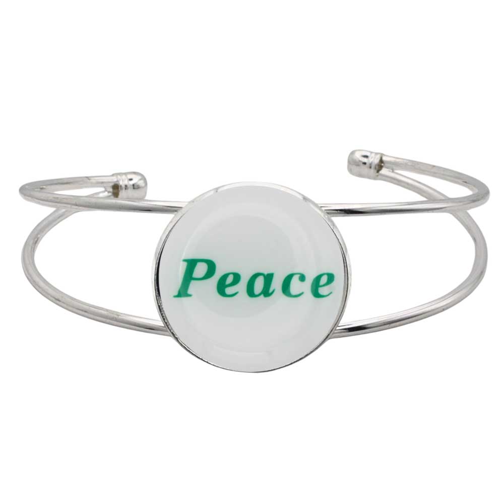 A silver-toned metal cuff bracelet featuring a round white disc with the word “Peace” printed in green script, shown on a plain white background – Lilylin Designs
