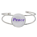 A silver-toned metal cuff bracelet featuring a round white disc with the word “Peace” printed in purple script, shown on a plain white background – Lilylin Designs