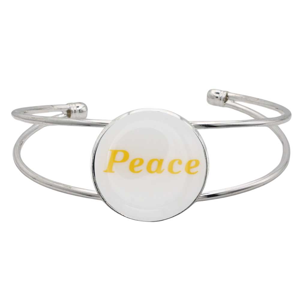 A silver-toned metal cuff bracelet featuring a round white disc with the word “Peace” printed in yellow script, shown on a plain white background – Lilylin Designs