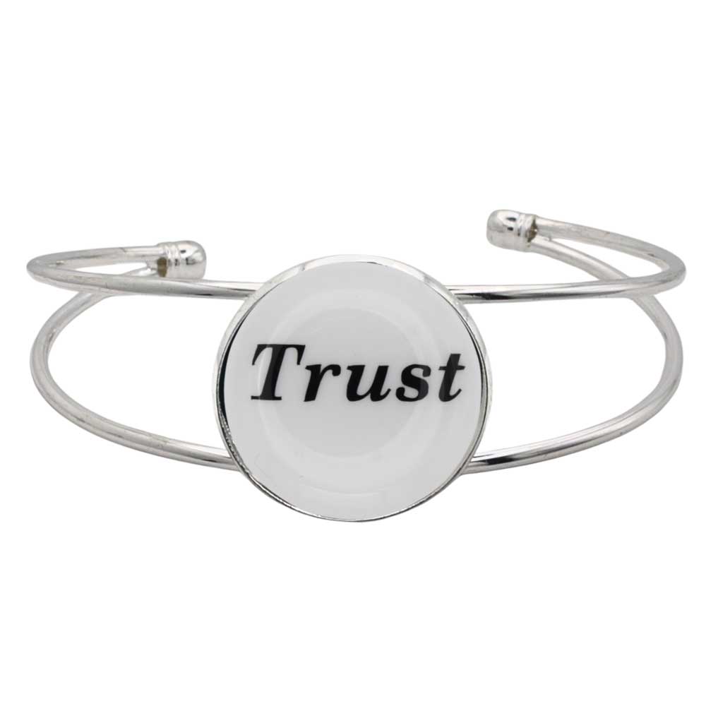 A silver-toned metal cuff bracelet featuring a round white disc with the word "Trust" printed in black script, shown on a plain white background – Lilylin Designs