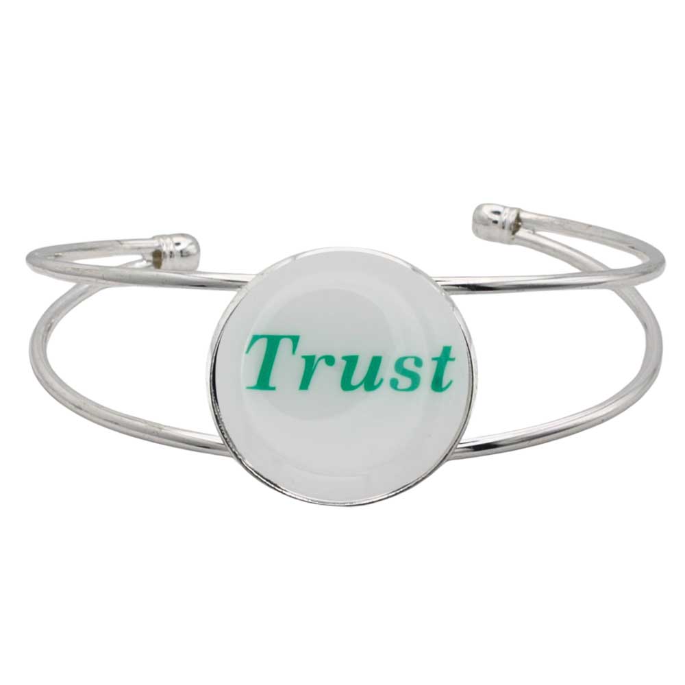 A silver-toned metal cuff bracelet featuring a round white disc with the word "Trust" printed in green script, shown on a plain white background – Lilylin Designs
