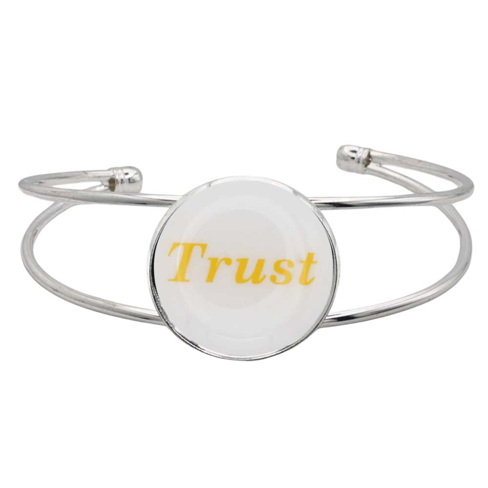 A silver-toned metal cuff bracelet featuring a round white disc with the word "Trust" printed in yellow script, shown on a plain white background – Lilylin Designs
