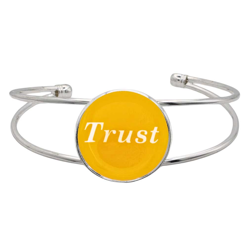 A silver-toned metal cuff bracelet featuring a round yellow disc with the word 'Trust' printed in white script, shown on a plain white background – Lilylin Designs